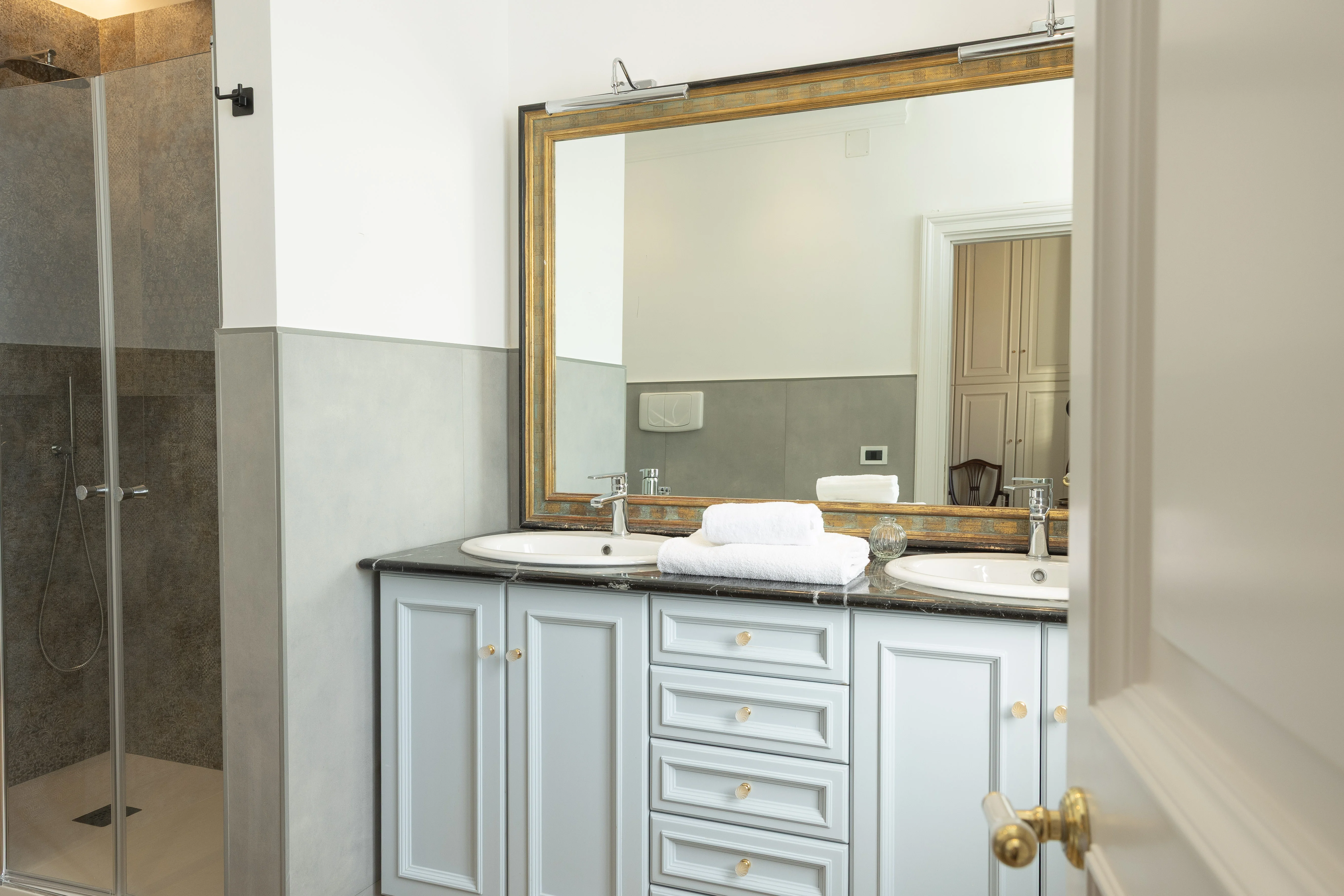 Bagno en suite con doppio lavabo, mobile grigio-azzurro e specchio cornice dorata